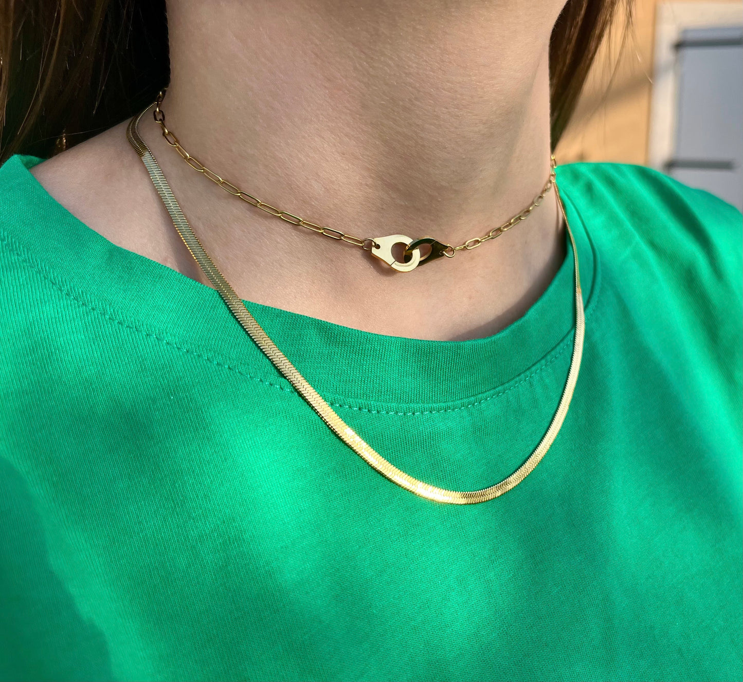 Cette photo représente une femme portant un collier menotté ras de cou doré. Ce collier est en acier inoxydable cela signifie qu'il est résistant à l'eau et qu'il ne ternit pas avec le temps. Ce collier est ajustable en ras de cou et représente deux menottes sui s'entrelacent. 